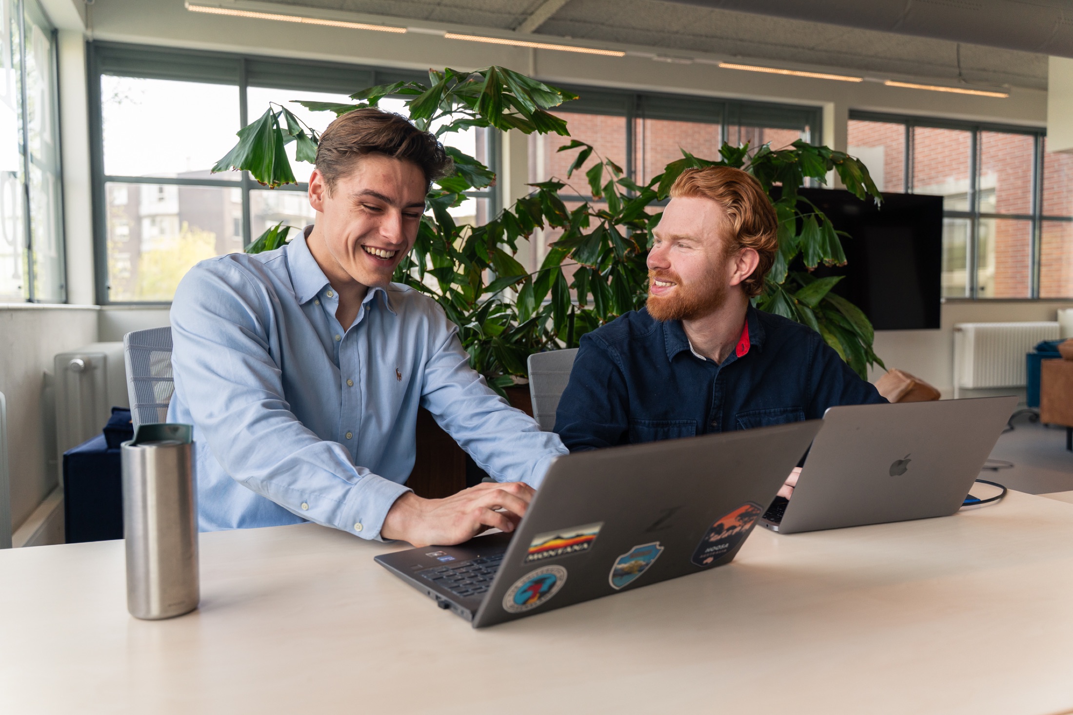 Twee collega's van BizzPower werken samen aan een laptop op kantoor